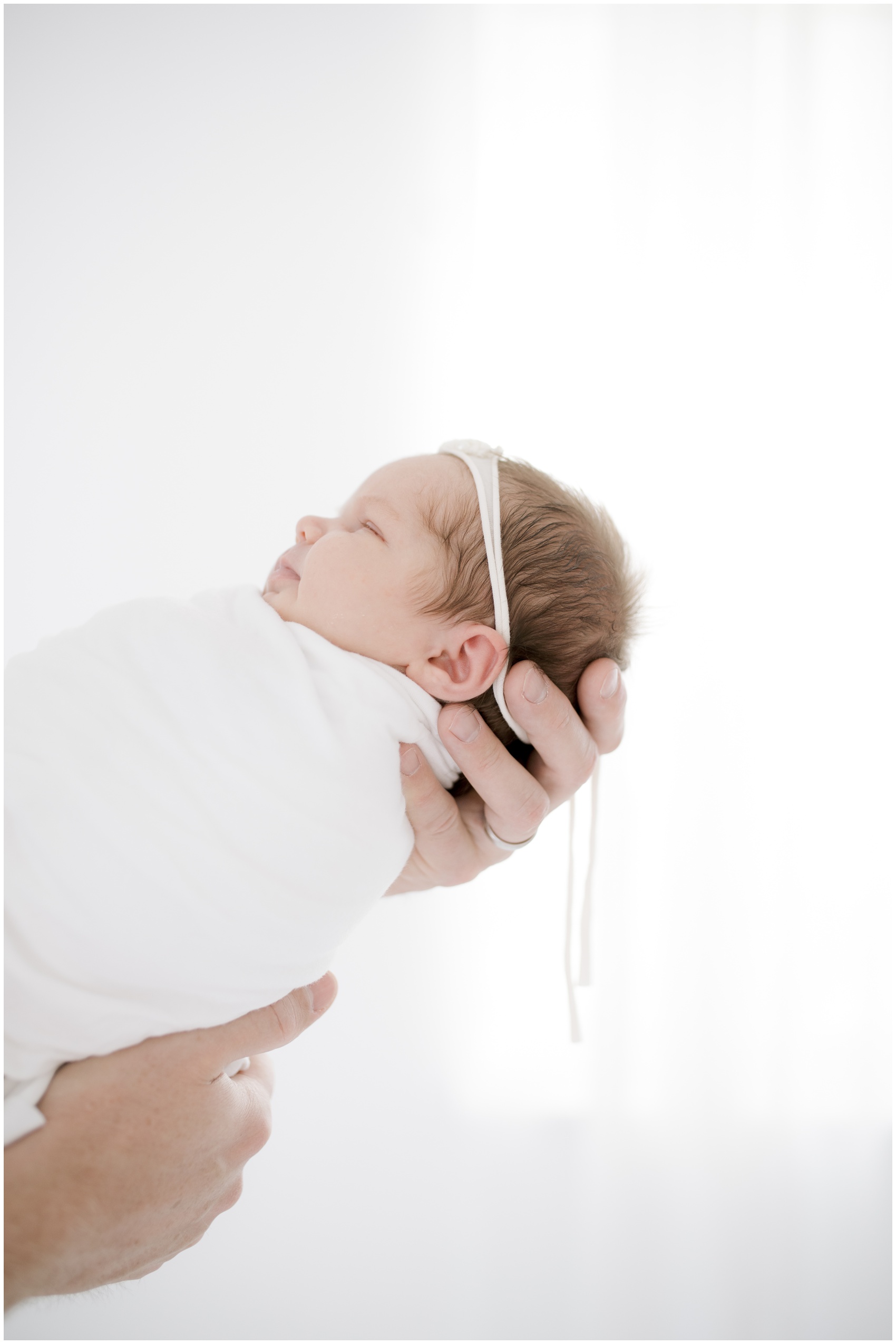 A newborn baby sleeps in dad's hands while standing in a window after meeting a night nurse in austin