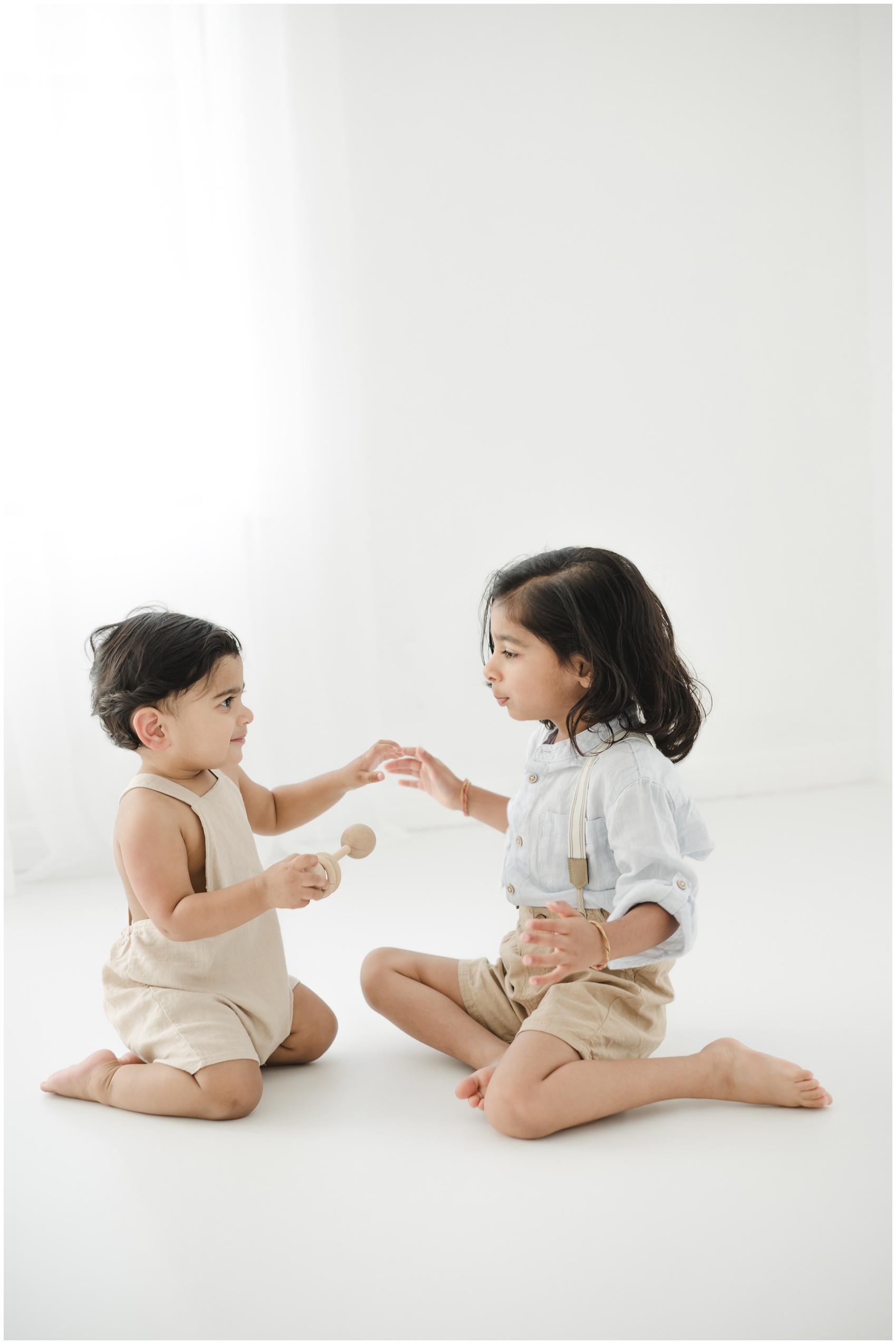 Toddler brothers kneel on the floor of a studio with wooden toys under a window after visiting toy stores in austin