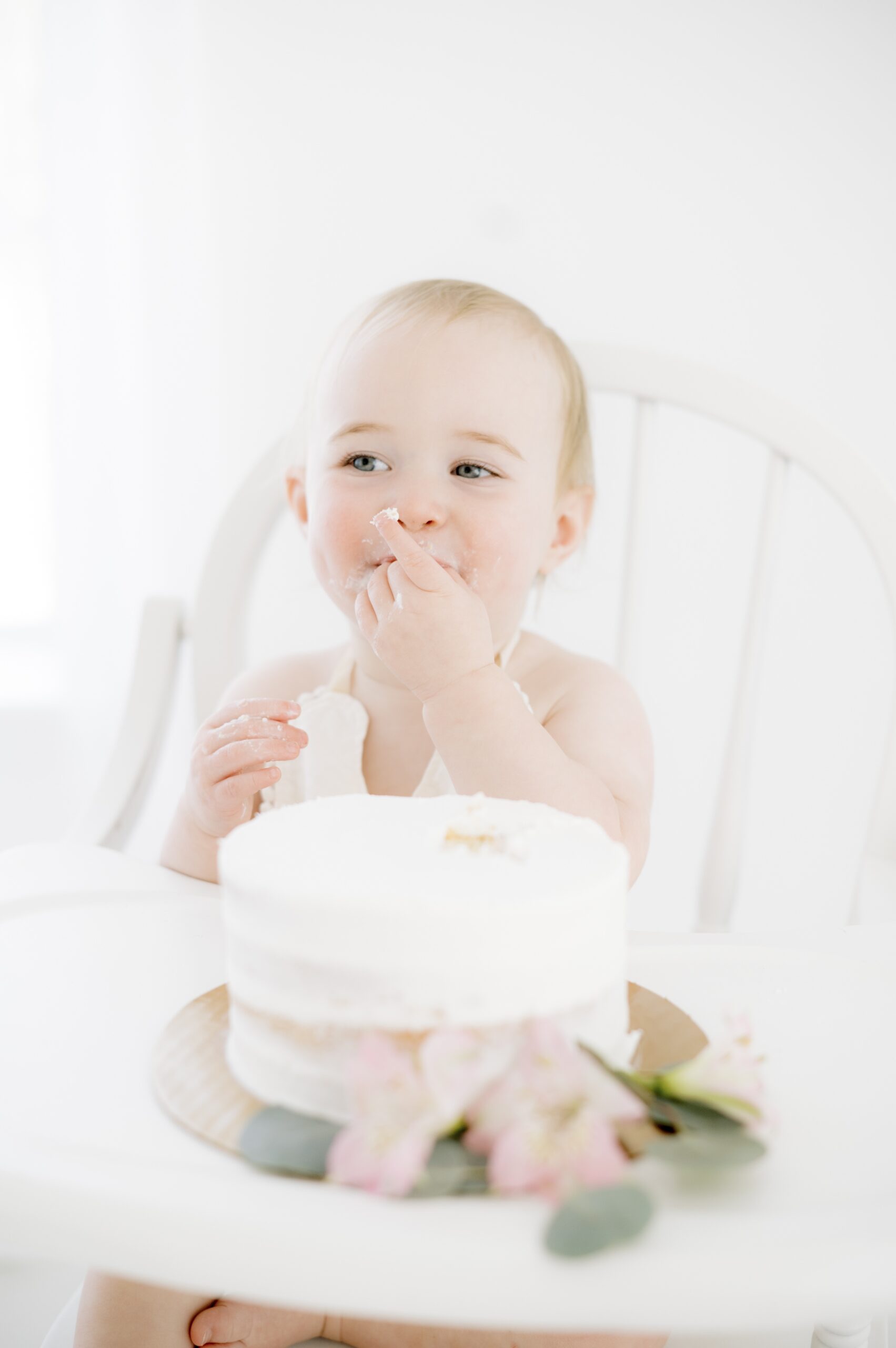 A happy baby sits in a white high chair smashing her white birthday cake before visiting an austin pediatric dentist