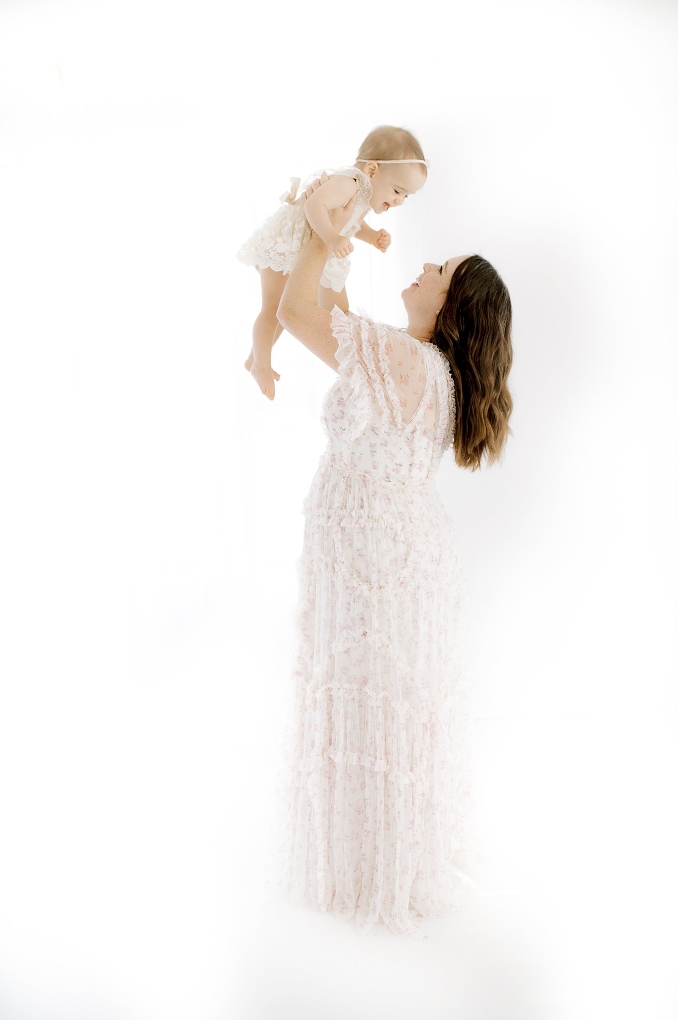 A mom in a lace dress lifts her baby above her head in a studio after exploring new year's eve in austin with kids