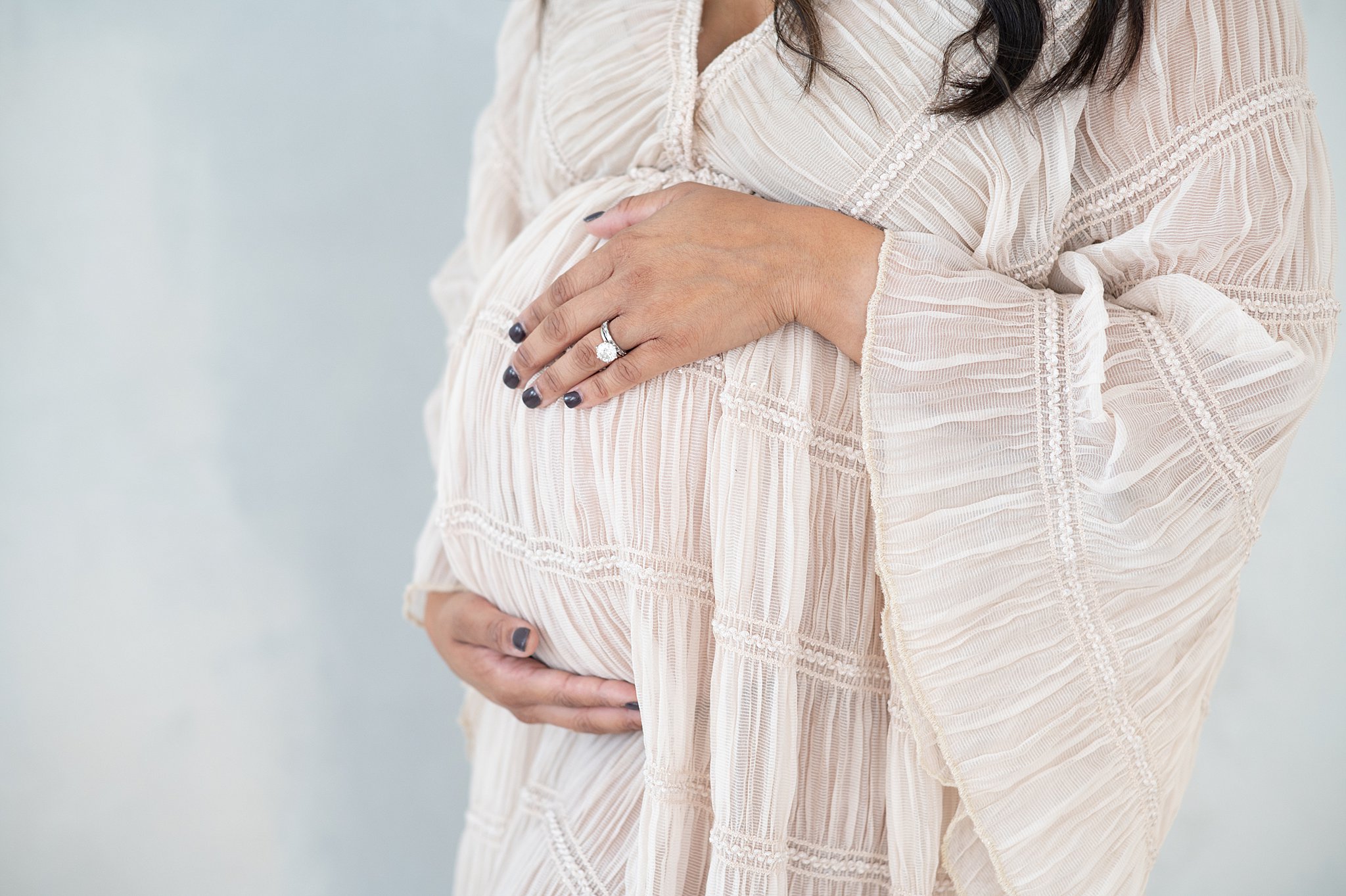 Details of a mom to be's bump with hands on it in a white gown after a prenatal massage in austin