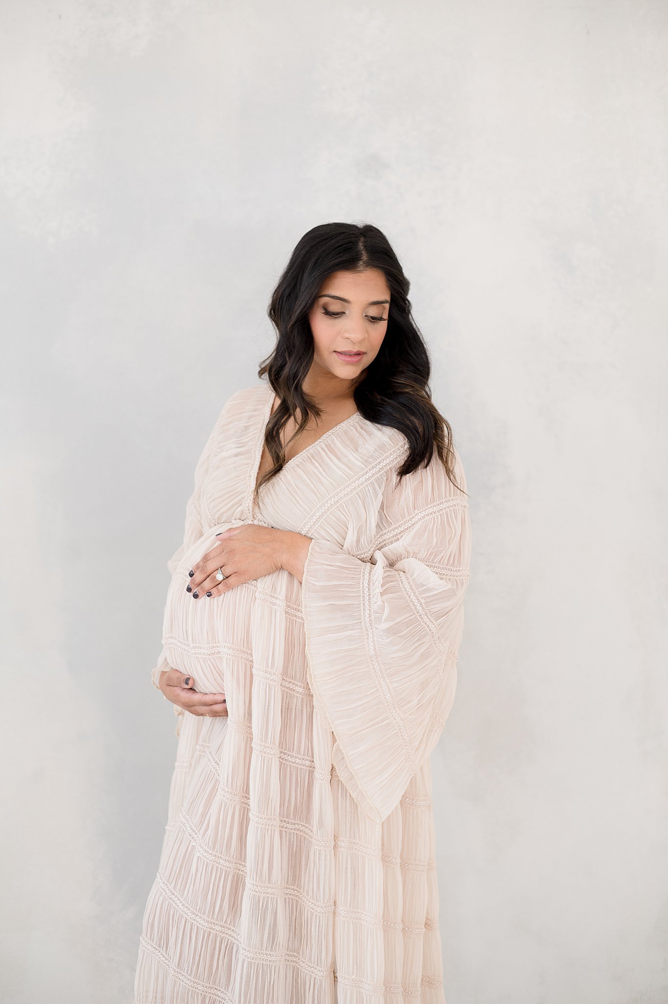 A mom to be walks in a studio in a pink maternity gown after a prenatal massage in austin